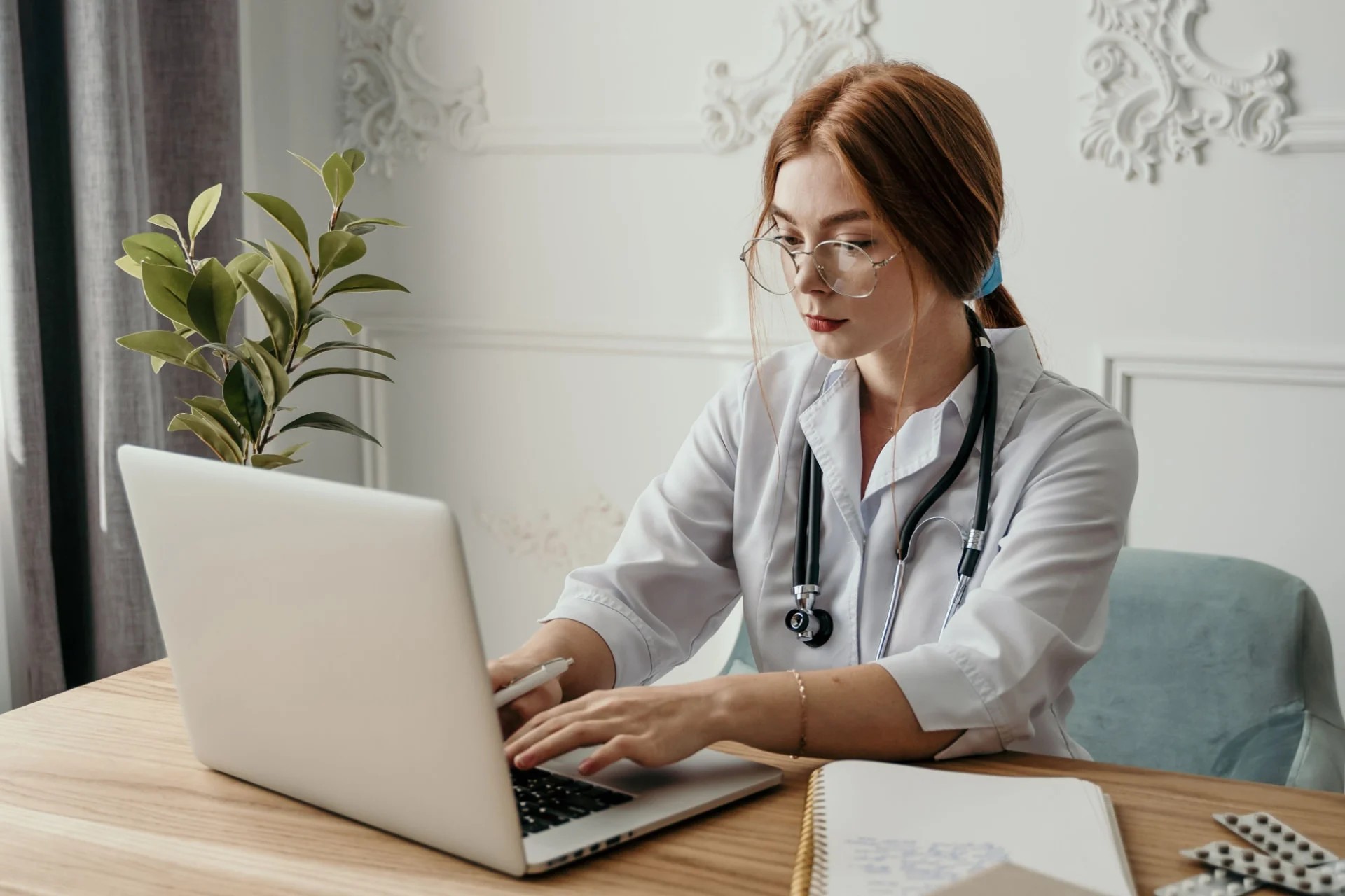 Clinical researcher in a white coat working on a laptop at a desk