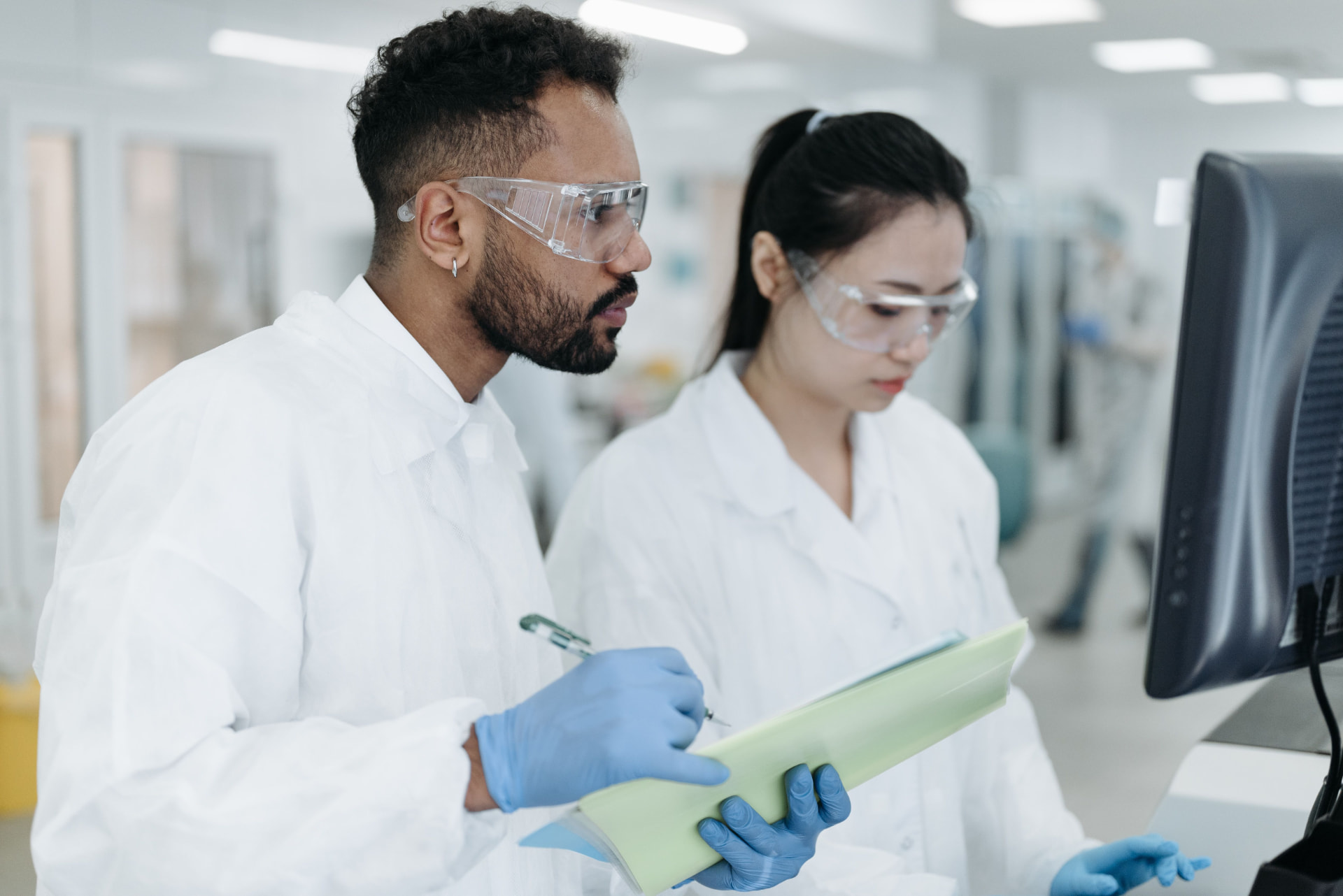 Clinical researchers reviewing study schedule documentation beside a laboratory monitor