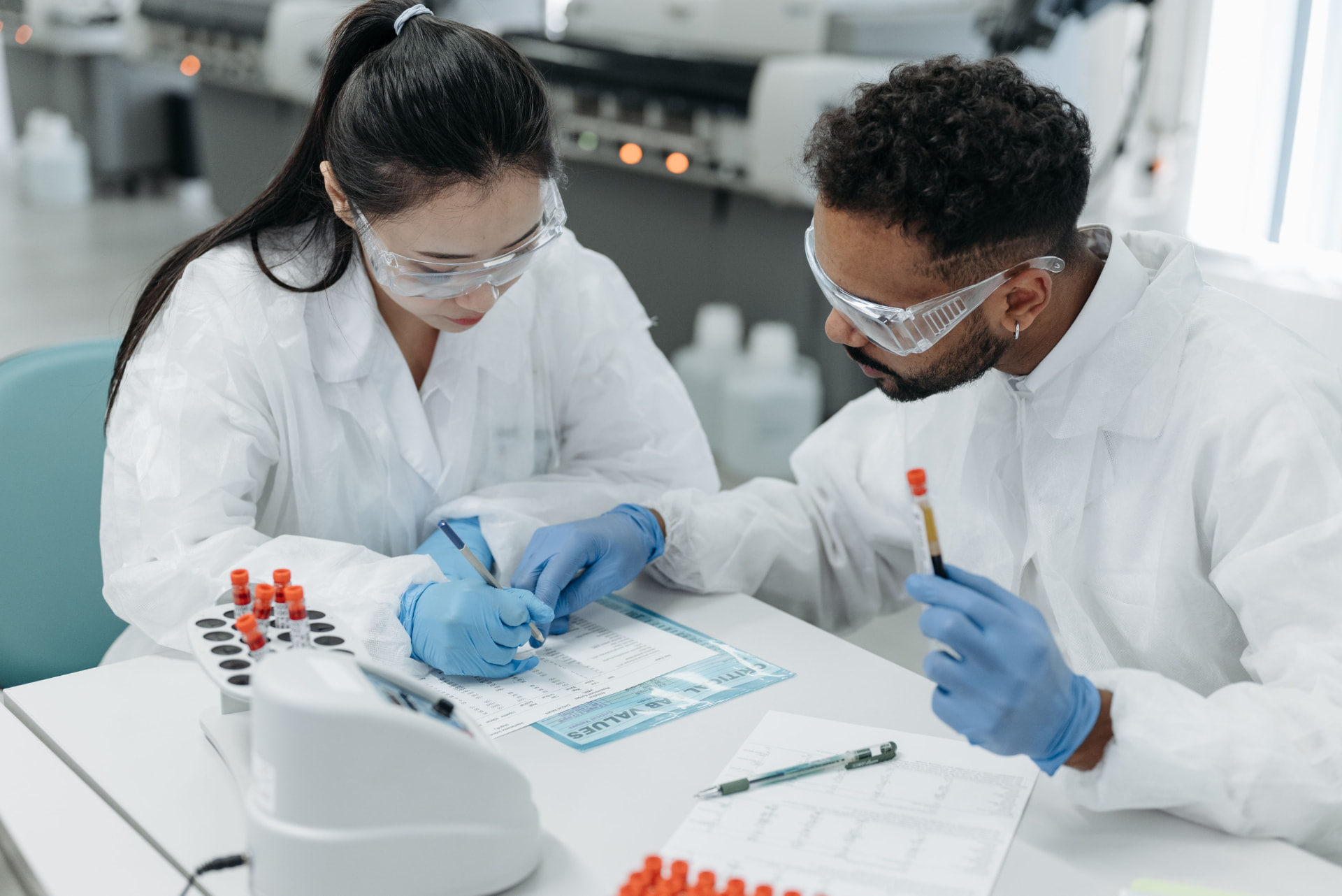 Two researchers in lab coats and protective eyewear reviewing clinical trial documentation in a laboratory